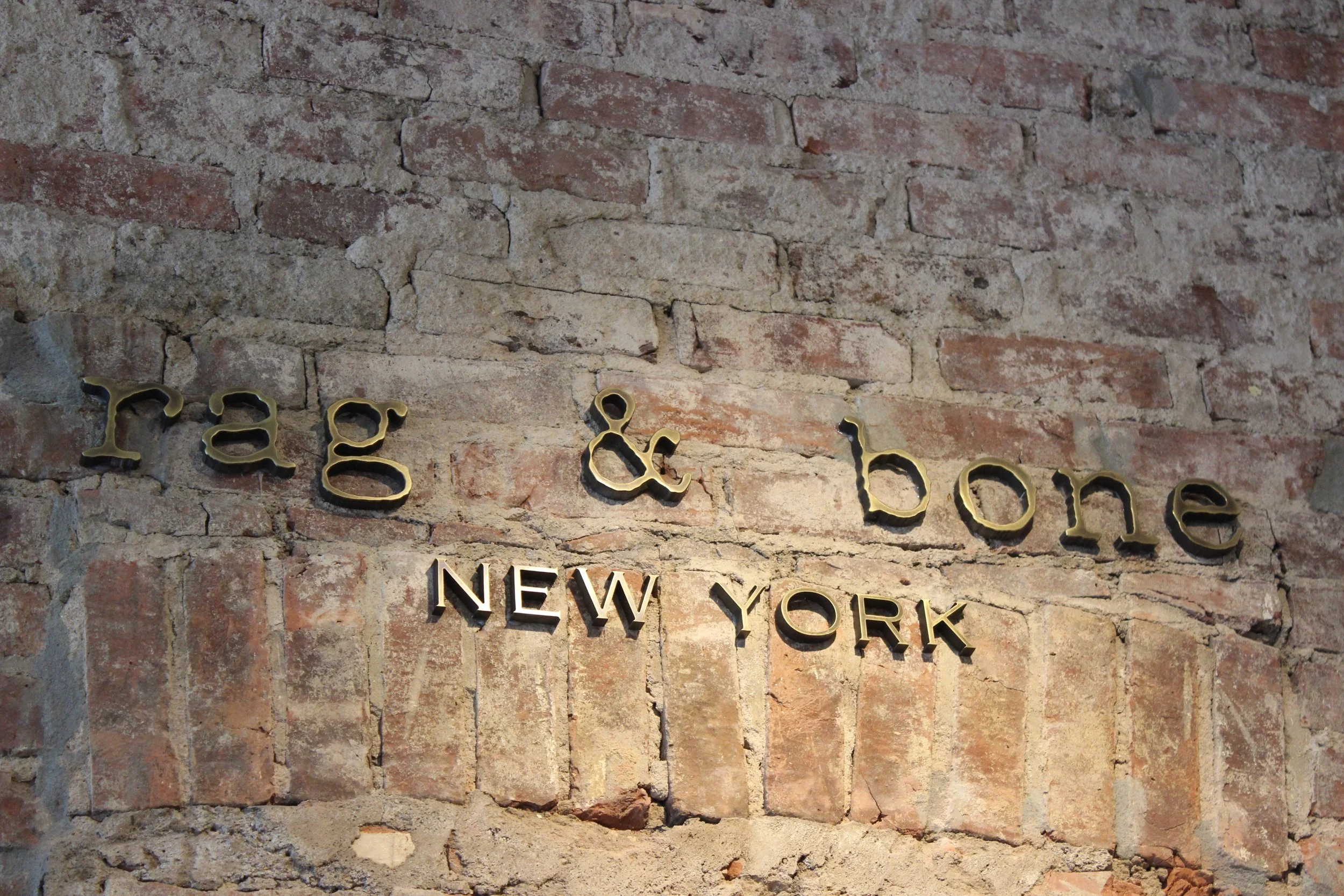 Close-up of Rag & Bone New York signage mounted on an exposed historic brick wall inside the retail store