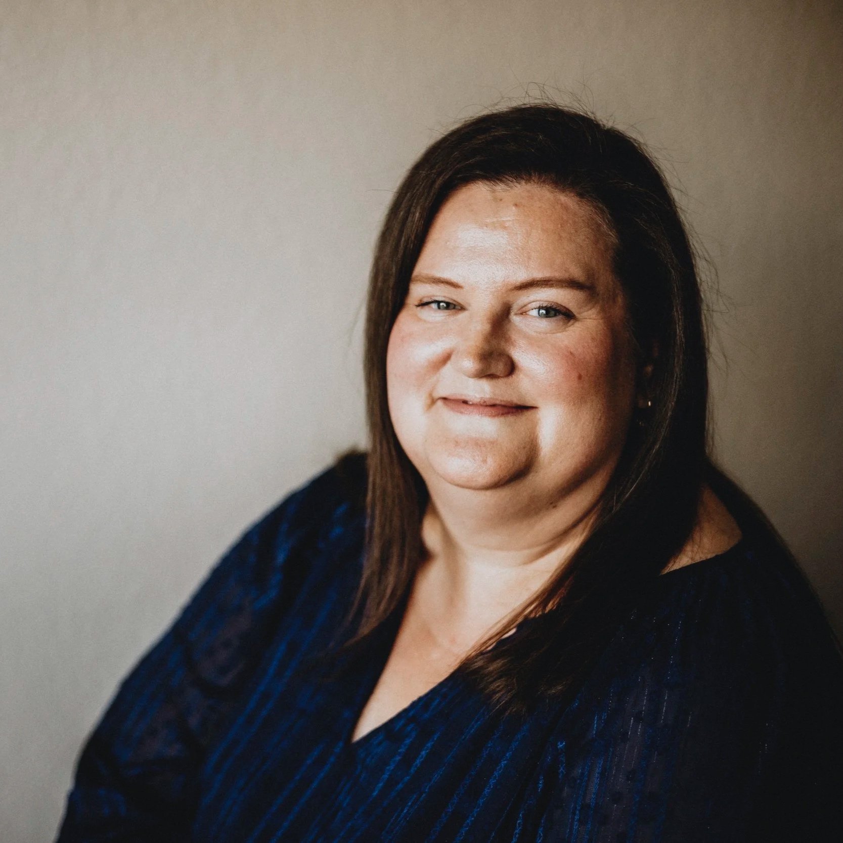 A woman with long brown hair and blue eyes smiling at the camera.