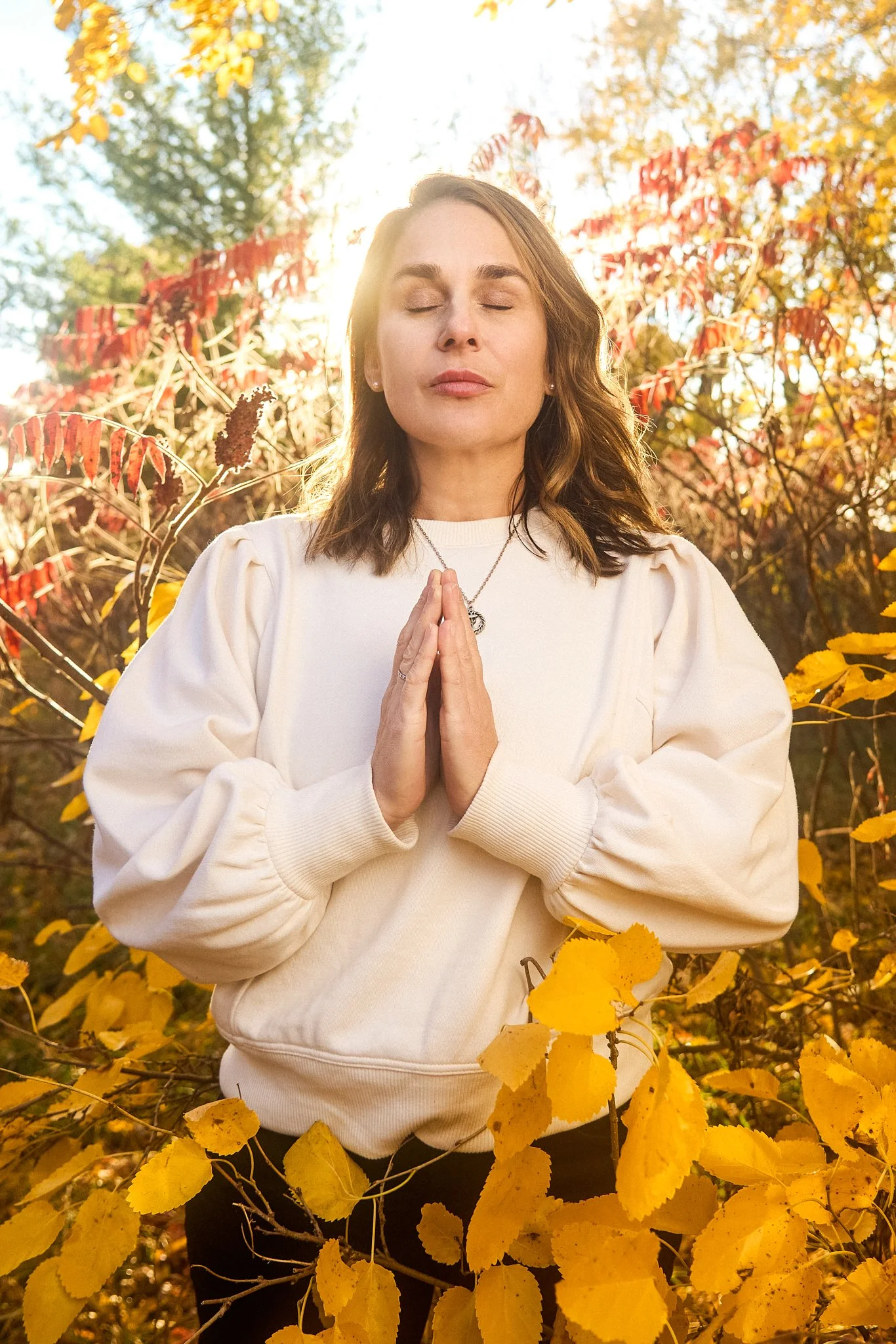 woman in prayer pose in yellow leaves