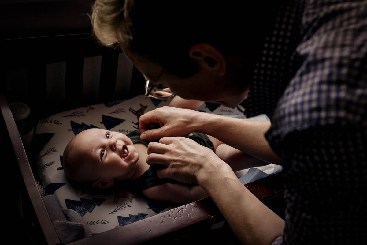 father tickles baby on change table