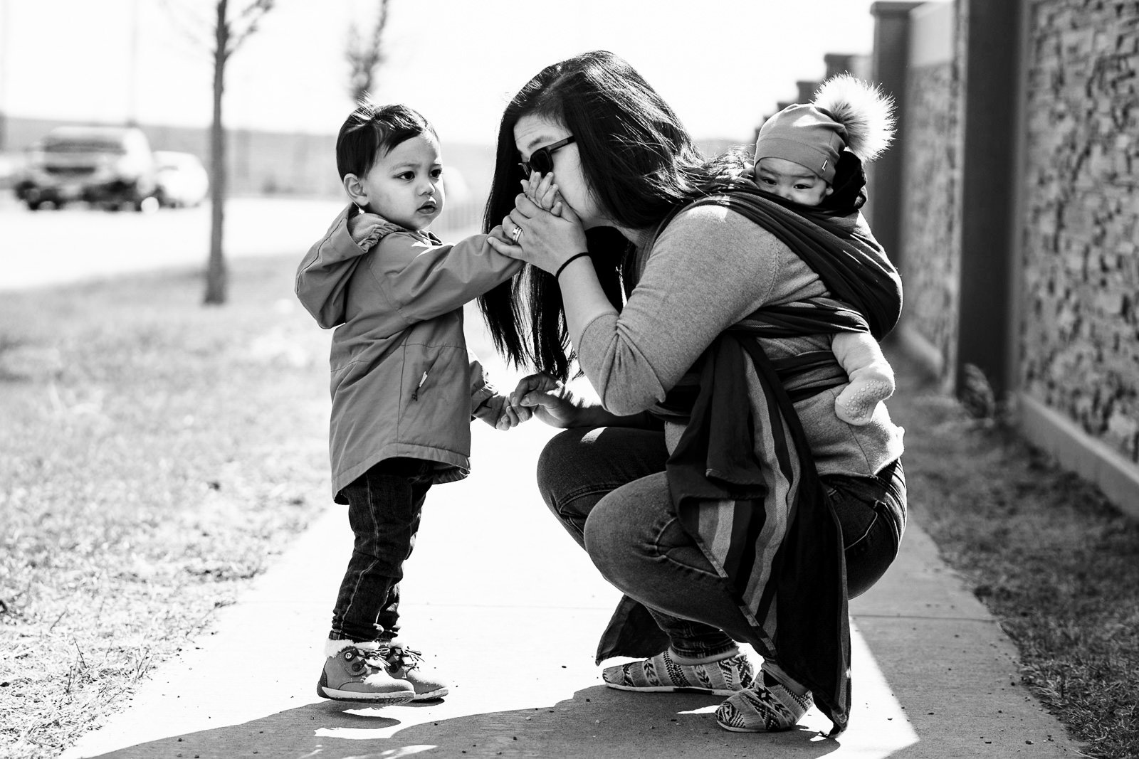mom kisses toddler hand while on walk and carrying baby