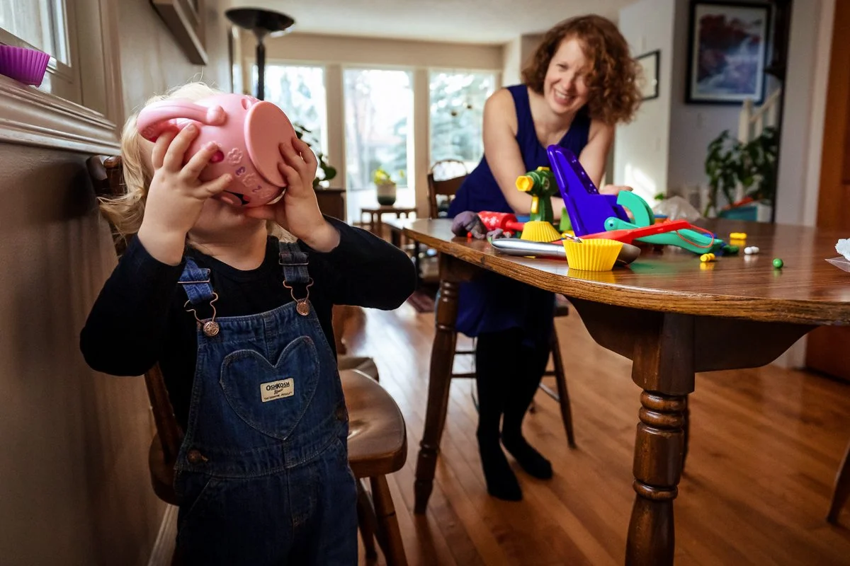 mother laughs as her toddler plays with his toys