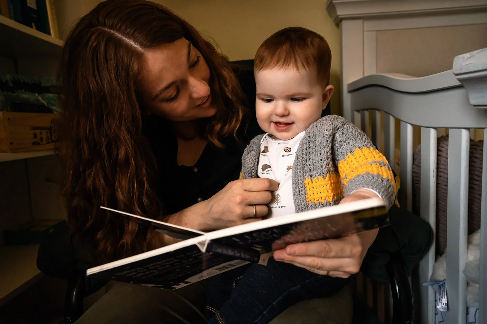 mother reading to baby girl by crib