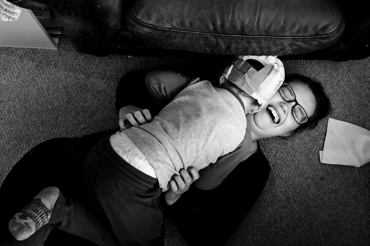 mom tacked by toddler with diaper on his head, mom laughing