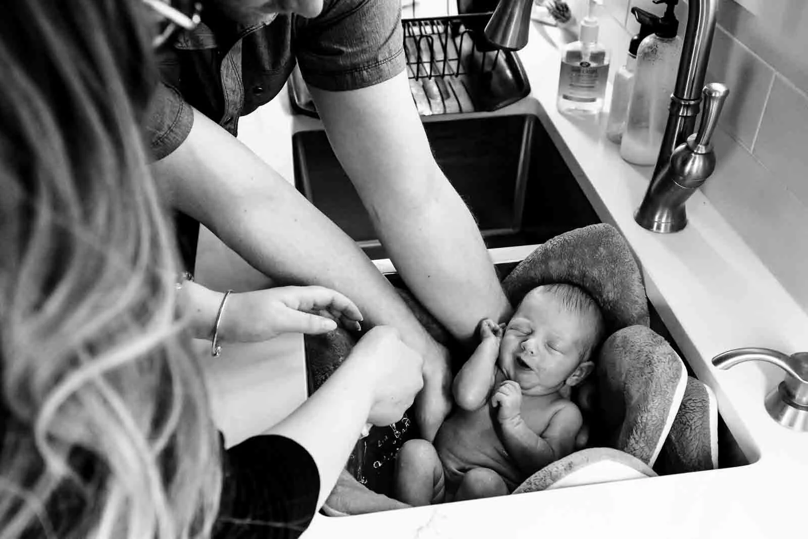 newborn baby getting a kitchen sink bath from both parents