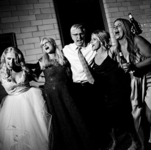 Group of five people singing and drinking at a party or celebration, standing close together and smiling.