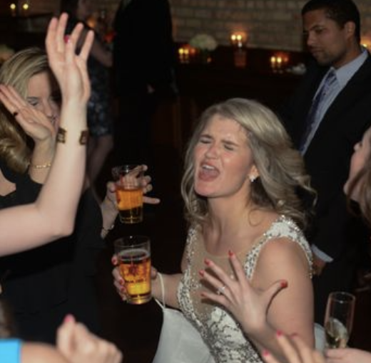 A woman with blonde hair in a white dress enjoying a drink and dancing at a party, with others around her holding drinks and dancing.