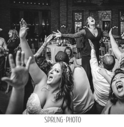 People dancing and celebrating at a party with a performer dressed as a mime or clown in the background.