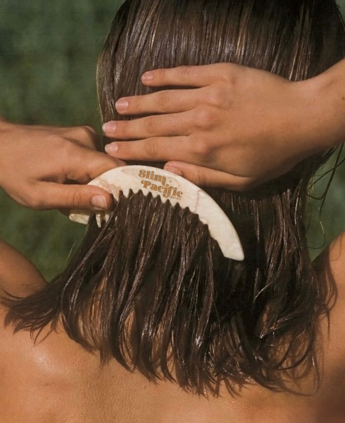 A person getting a hair treatment, with a hairbrush labeled 'Slim Pacific Salon' being used on wet, dark brown hair.