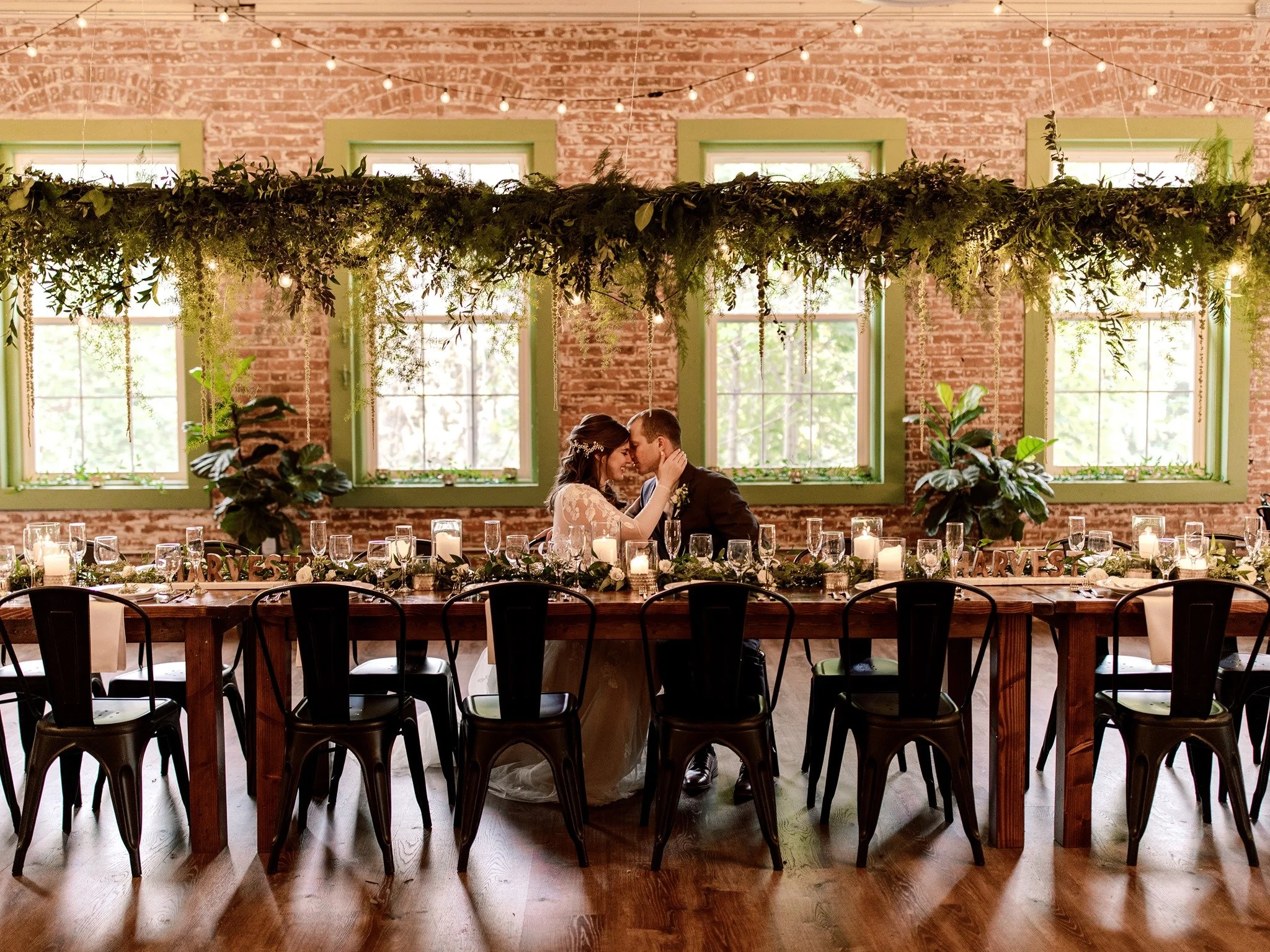 Bride and groom seated at a long table embraced.