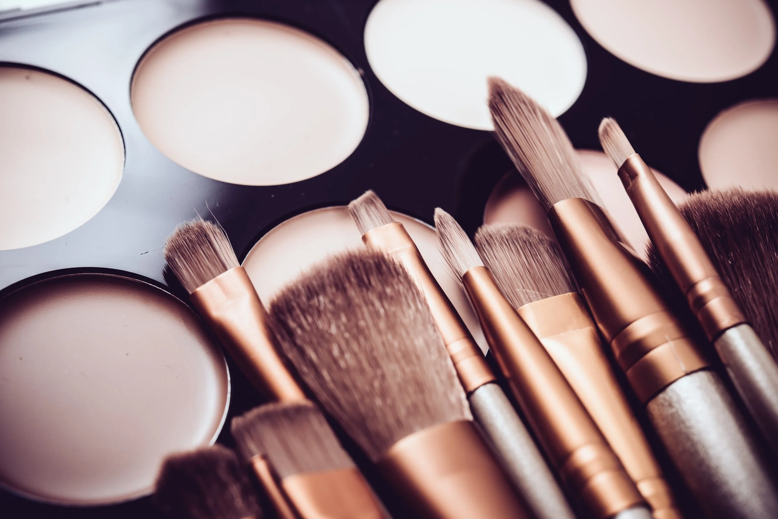A collection of makeup brushes resting on a palette of cream and brown powders.