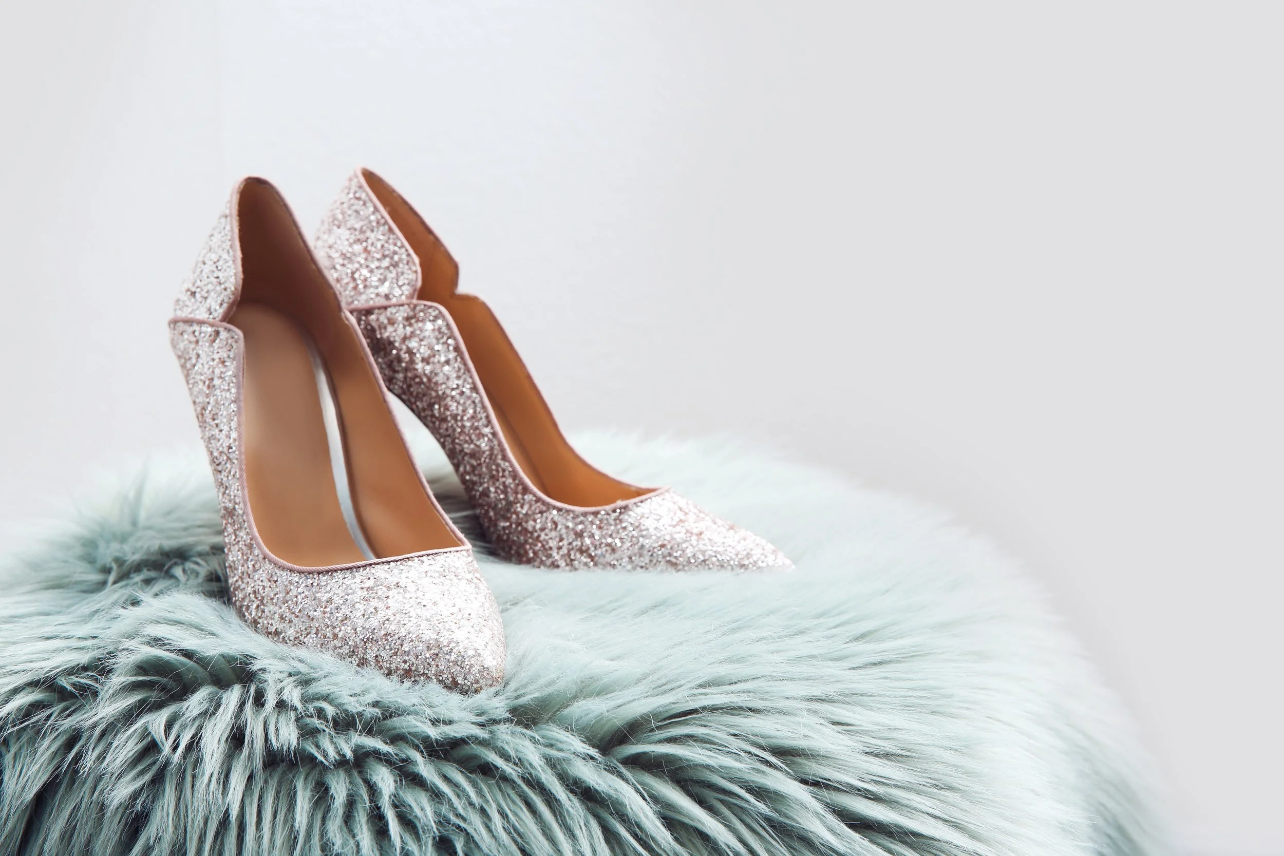 A pair of glittery pink high-heeled shoes on a fluffy surface.