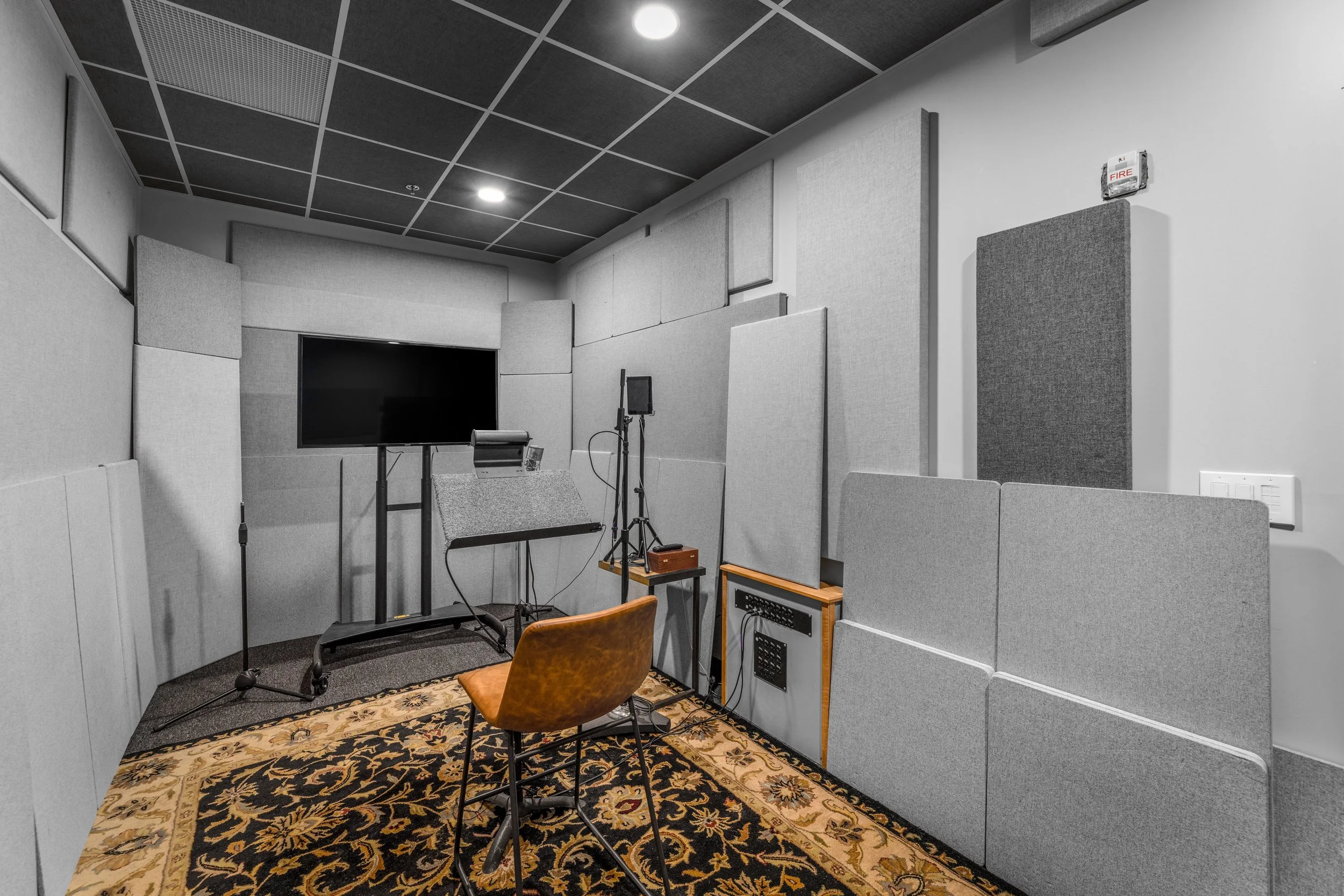 Recording studio with soundproofing panels, a television, a chair, and audio equipment on a patterned rug.