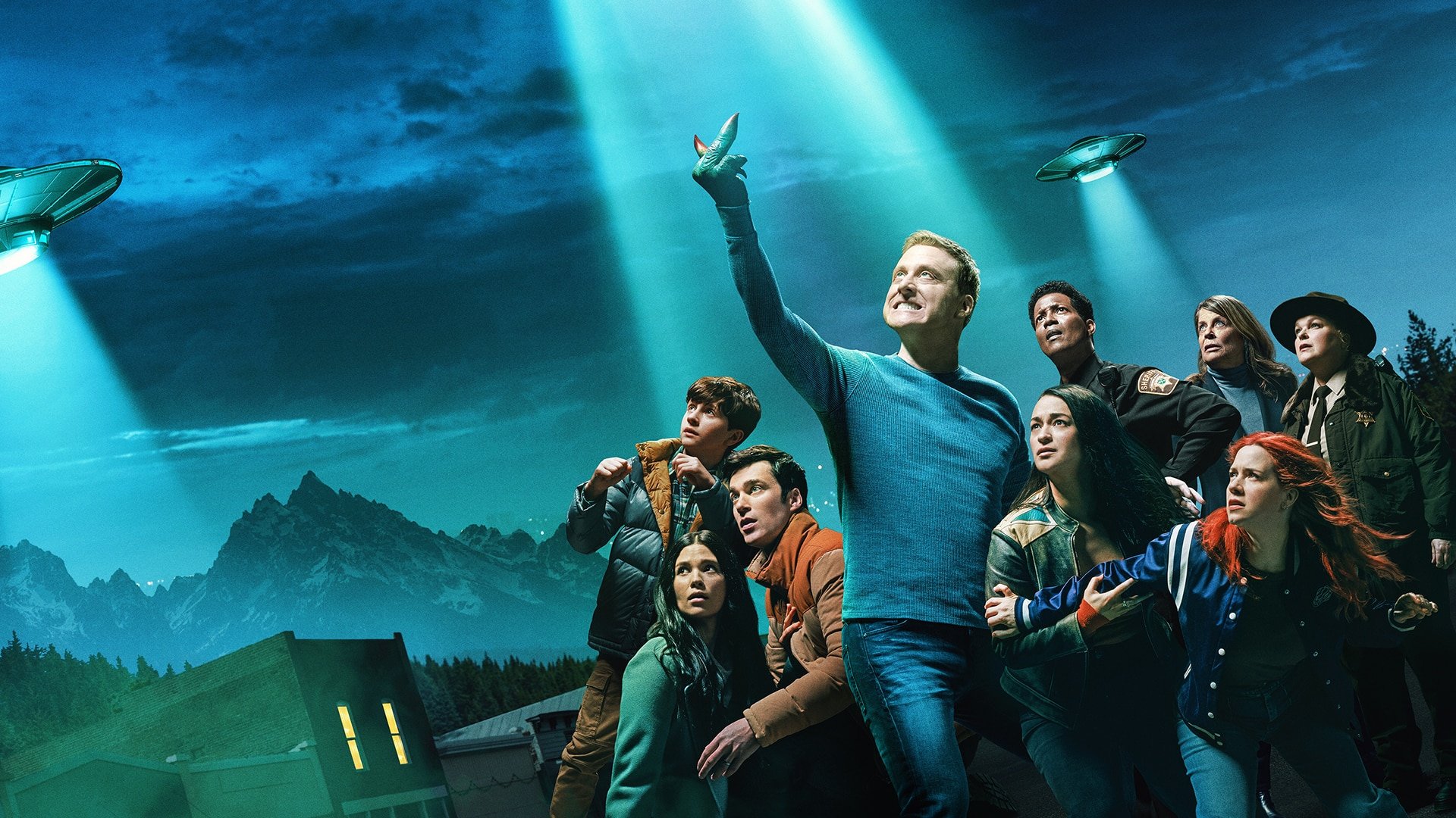 Group of people looking up at UFO in the night sky with mountains in the background.