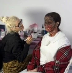 A woman with make-up and glasses applying makeup to another woman with a makeup sponge in a salon or makeup studio.