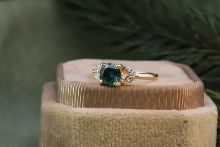 custom green stone ring with round rose cut emerald center stone and marquise diamonds on the side made of yellow gold placed on velvet pink ring box