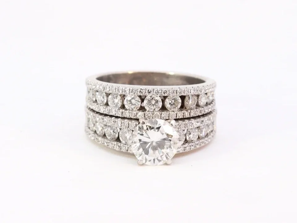 white gold diamond ring set pavé and channel set, with a round diamond center stone and matching band, on a white background