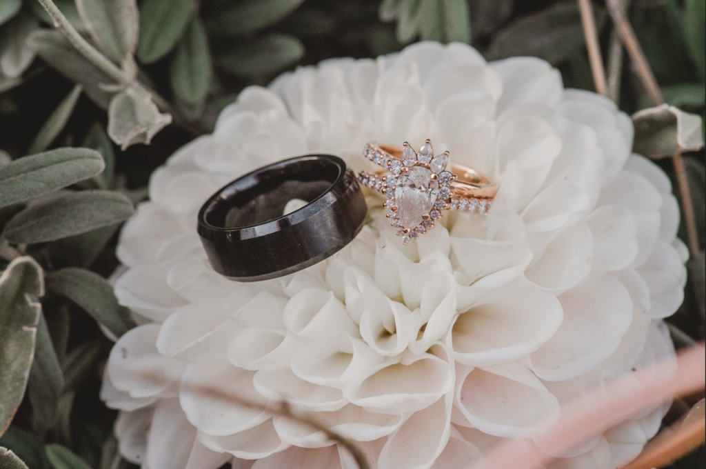  a black men’s band and a custom rose gold engagement ring on a flower 