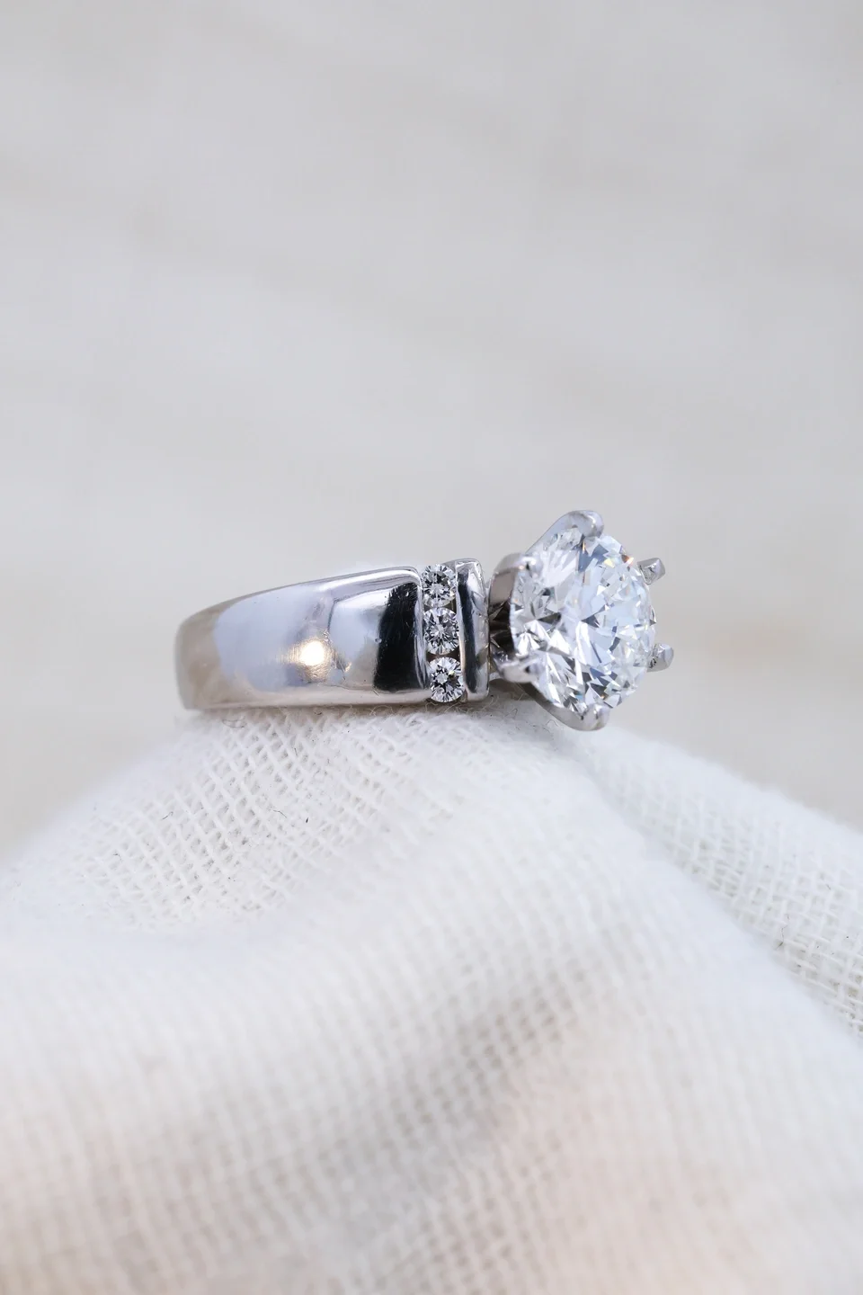 White gold engagement ring with thick band and channel set side diamonds, round center stone