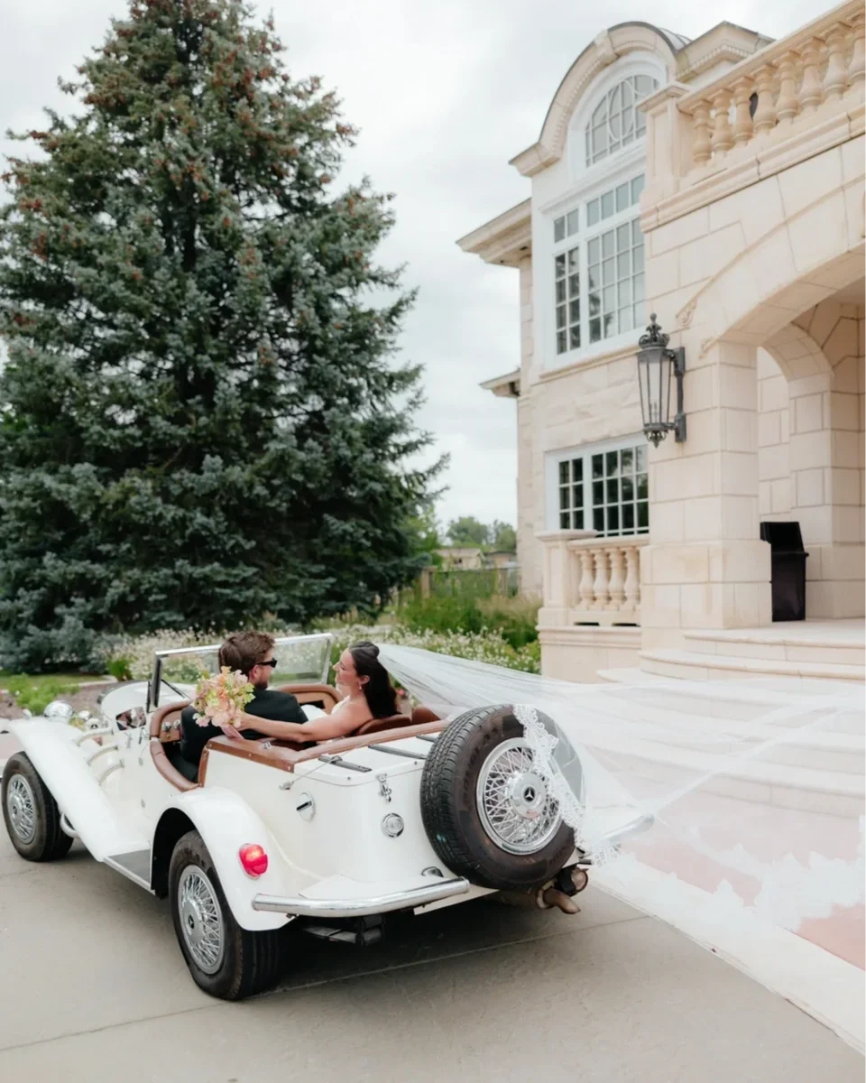 bride and groom in car facing away driving away from reception with veil flowing