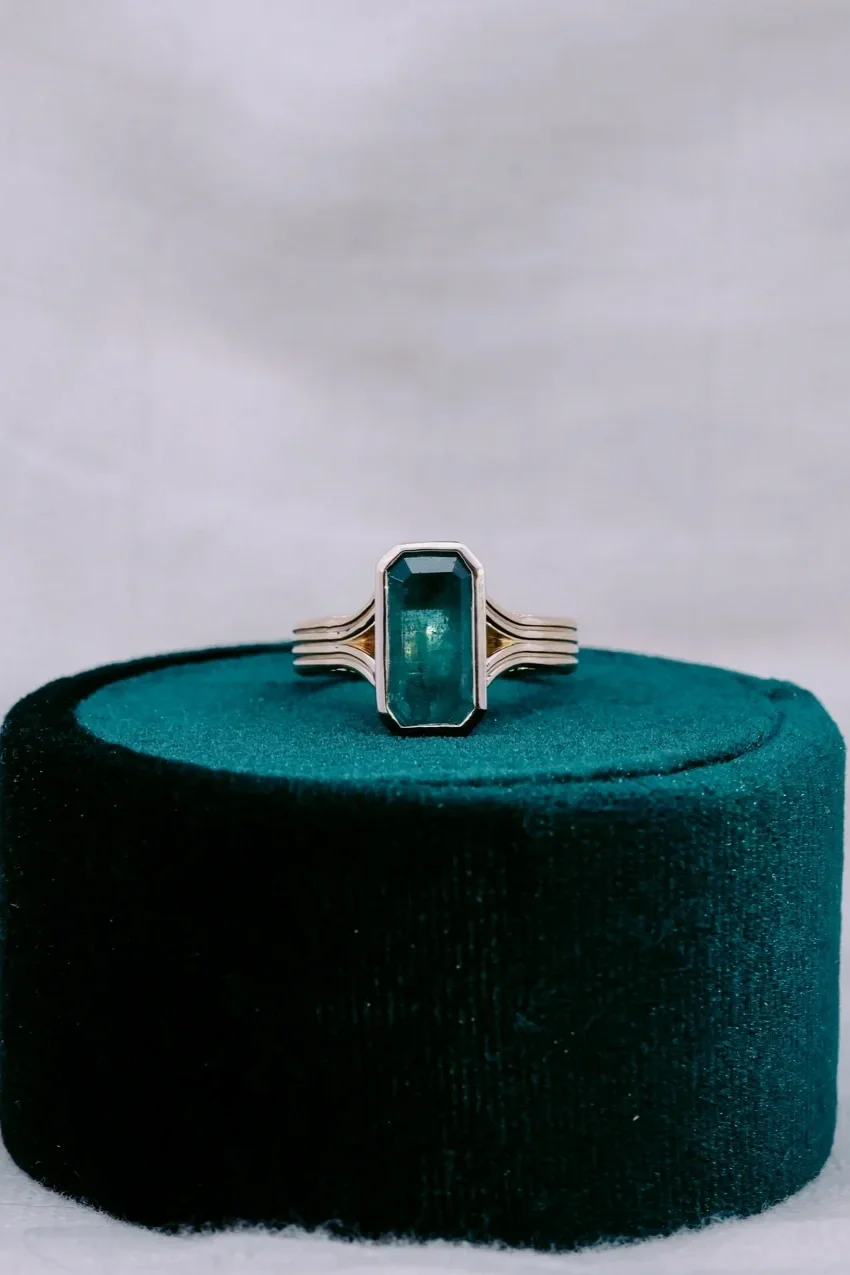 Custom cut emerald in bezel set custom yellow gold solitaire ring split shank on velvet green ring box