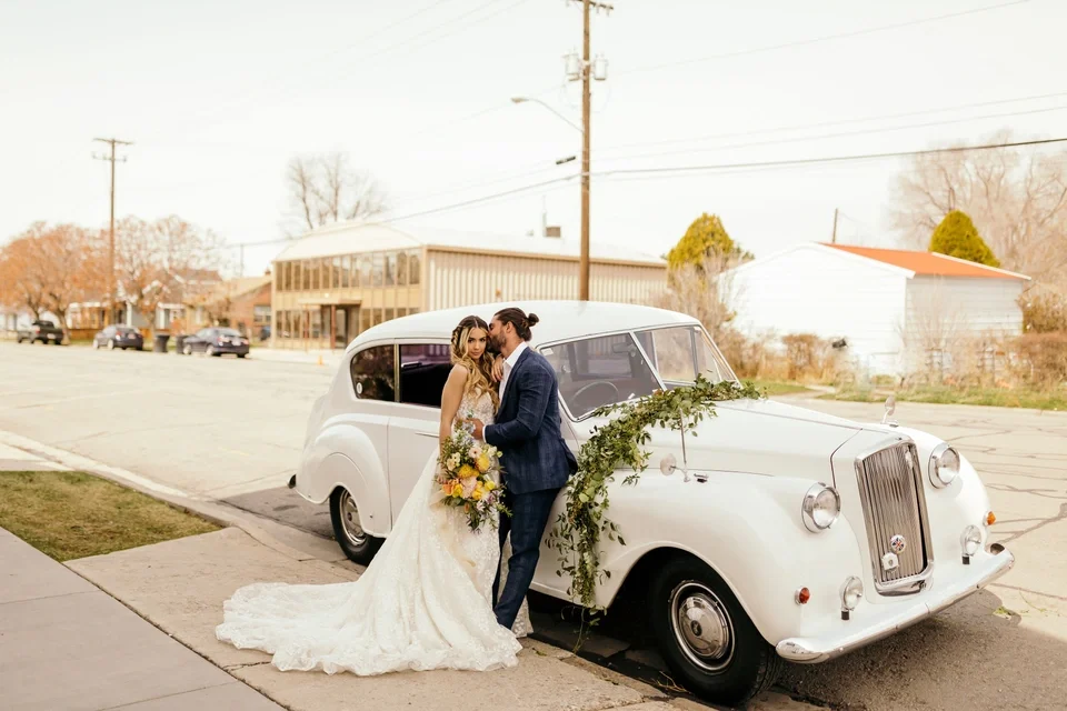 bride and groom standing by vintage white car in summer