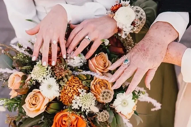 bride, mother, and grandmother holding hands with rings over bouquet, including diamonds, sapphires, and turquoise, rose gold, white gold, and silver