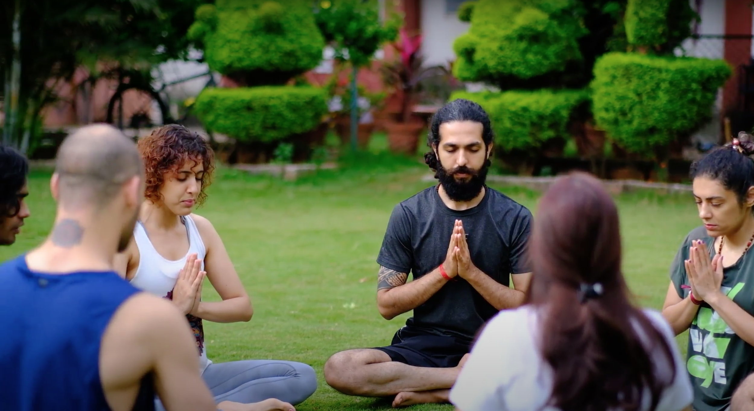 Participants in seated meditation with palms joined on the lawn at a Yukah programme.