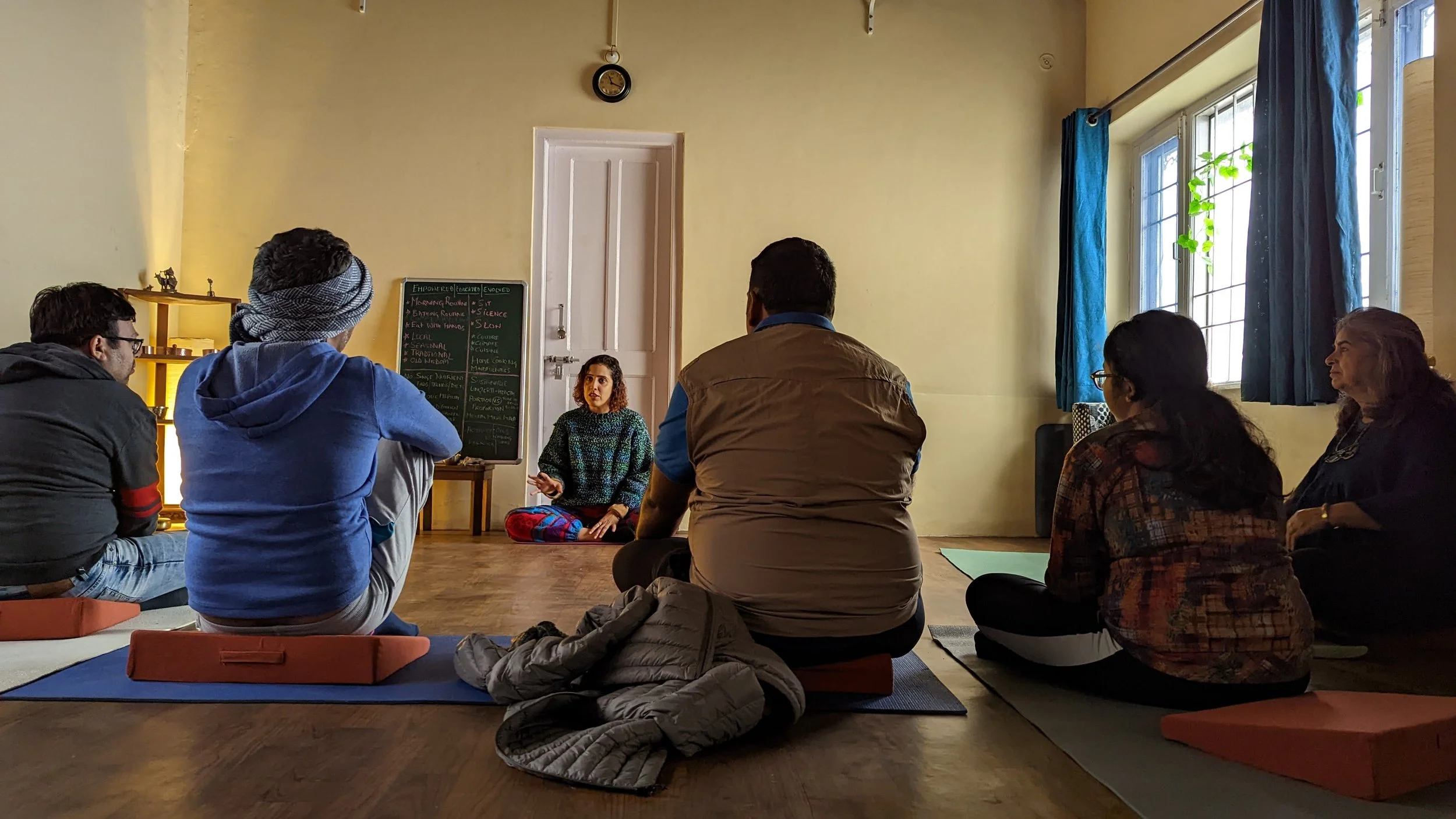 Participants seated on cushions for a morning talk in a sunlit room at a Yukah programme.