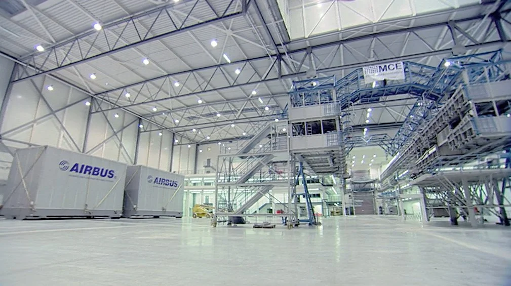 Innenansicht einer großen Halle mit "Airbus"-Containern und industriellen Anlagen.