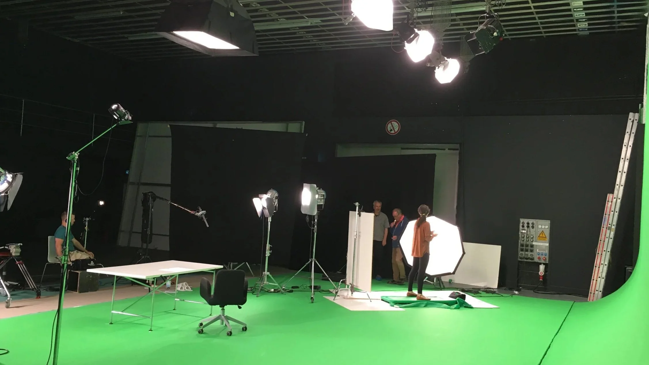 Filmstudio mit grünem Hintergrund, Beleuchtung und Kameraequipment.