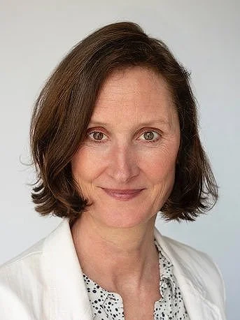 Porträt einer Frau mit schulterlangem braunem Haar in einem weißen Blazer.
