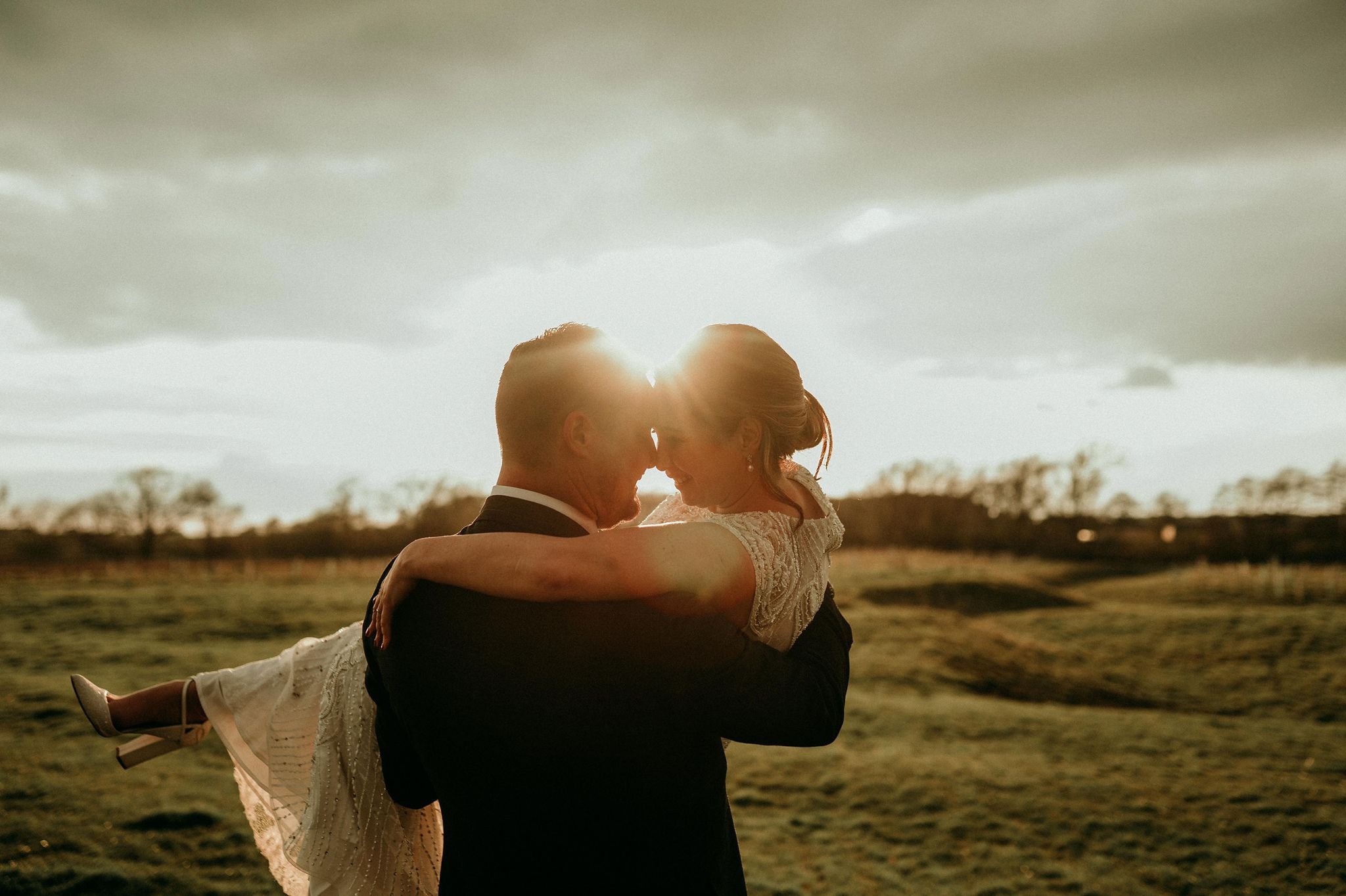 groom carrying bride in sunny field