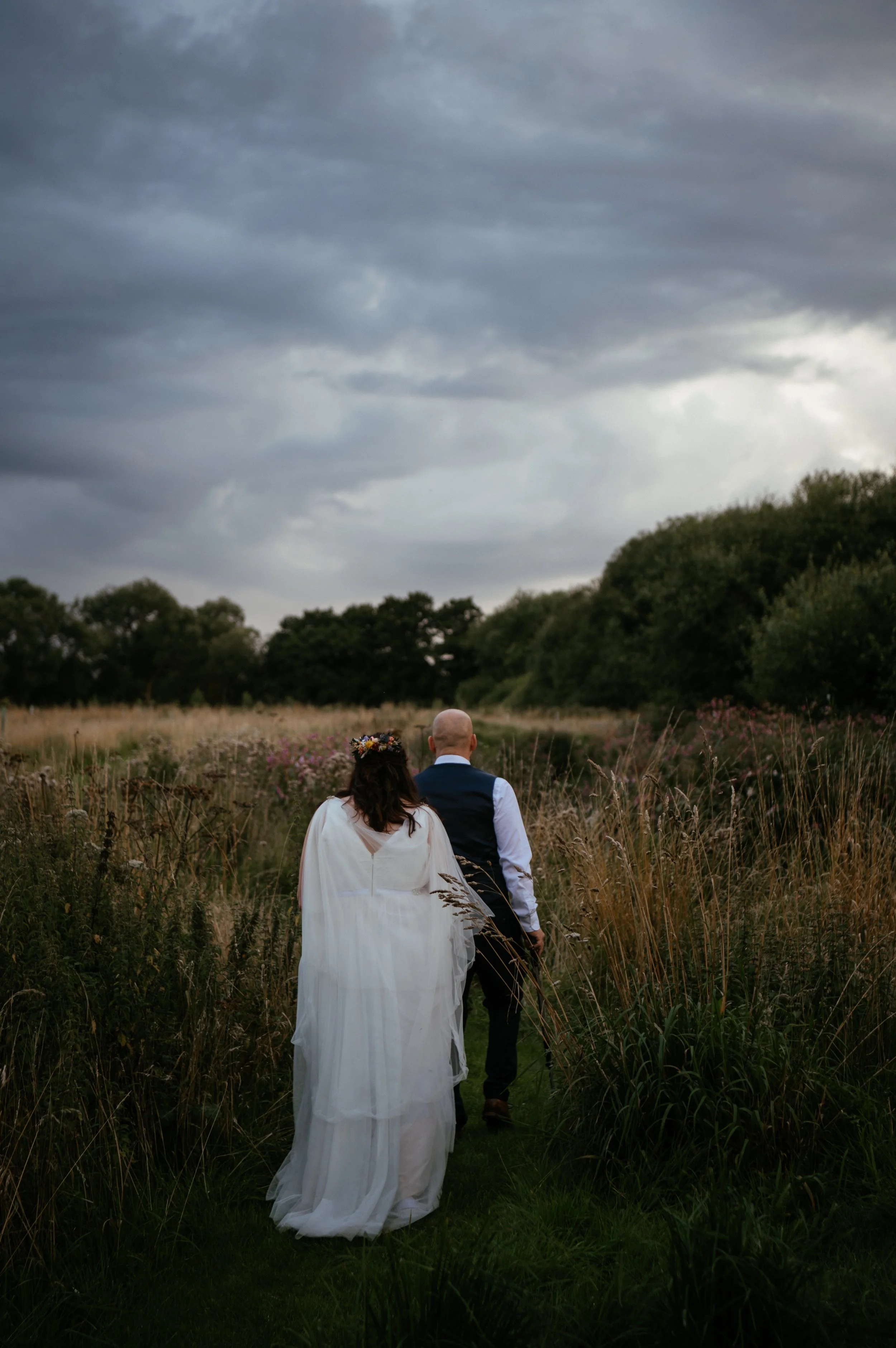 bride and groom walking away through field