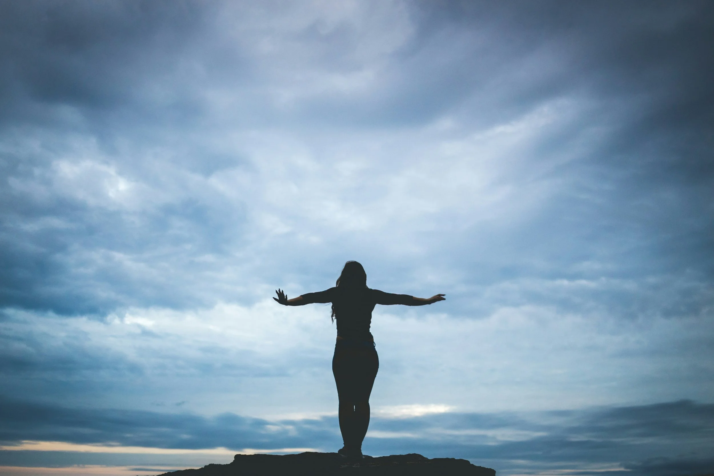 A woman balancing on a peak to illustrate being in the Window of Tolerance, handling emotions while staying present.
