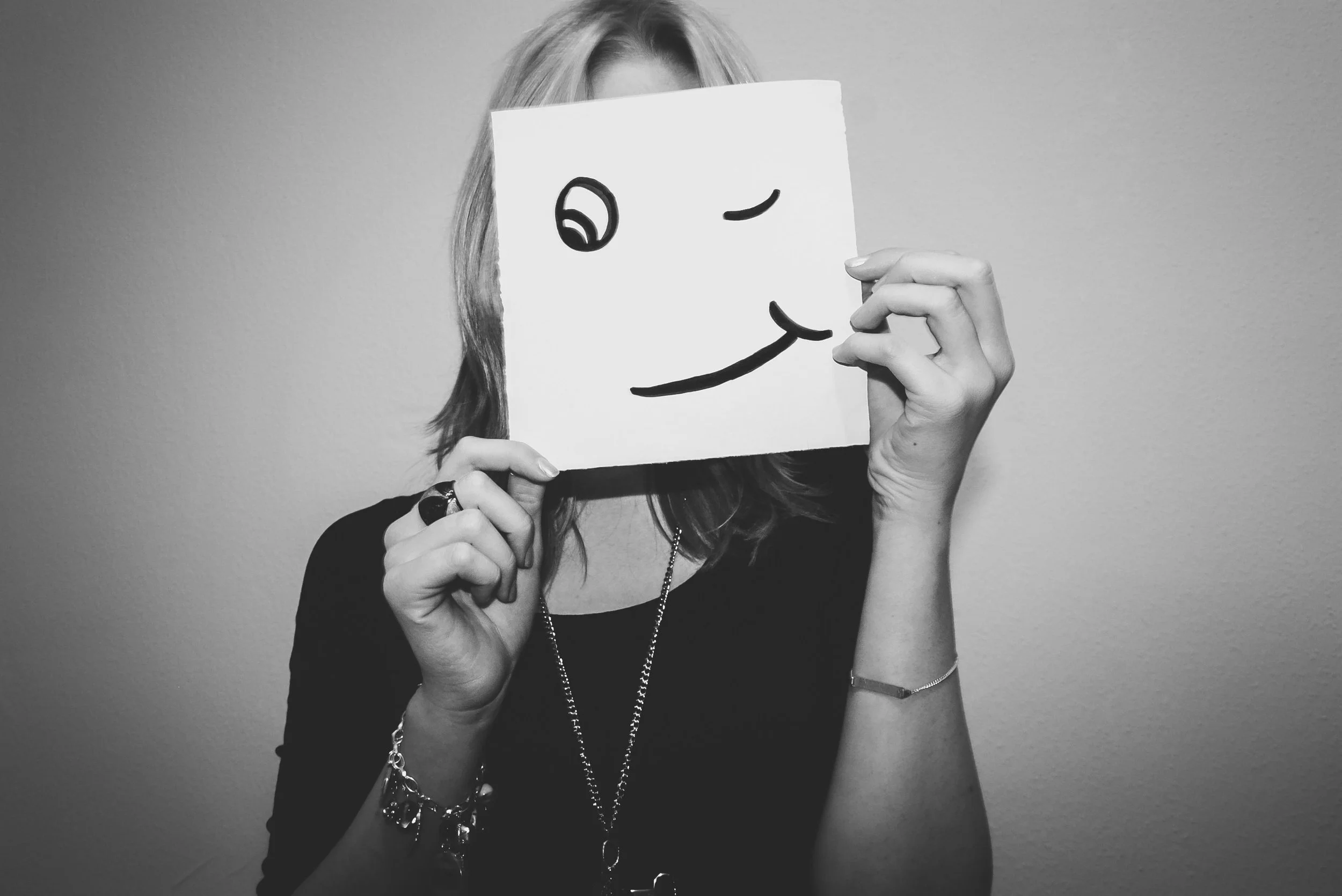 An image of a woman holding up a drawing of a happy face to demonstrate imposter syndrom.