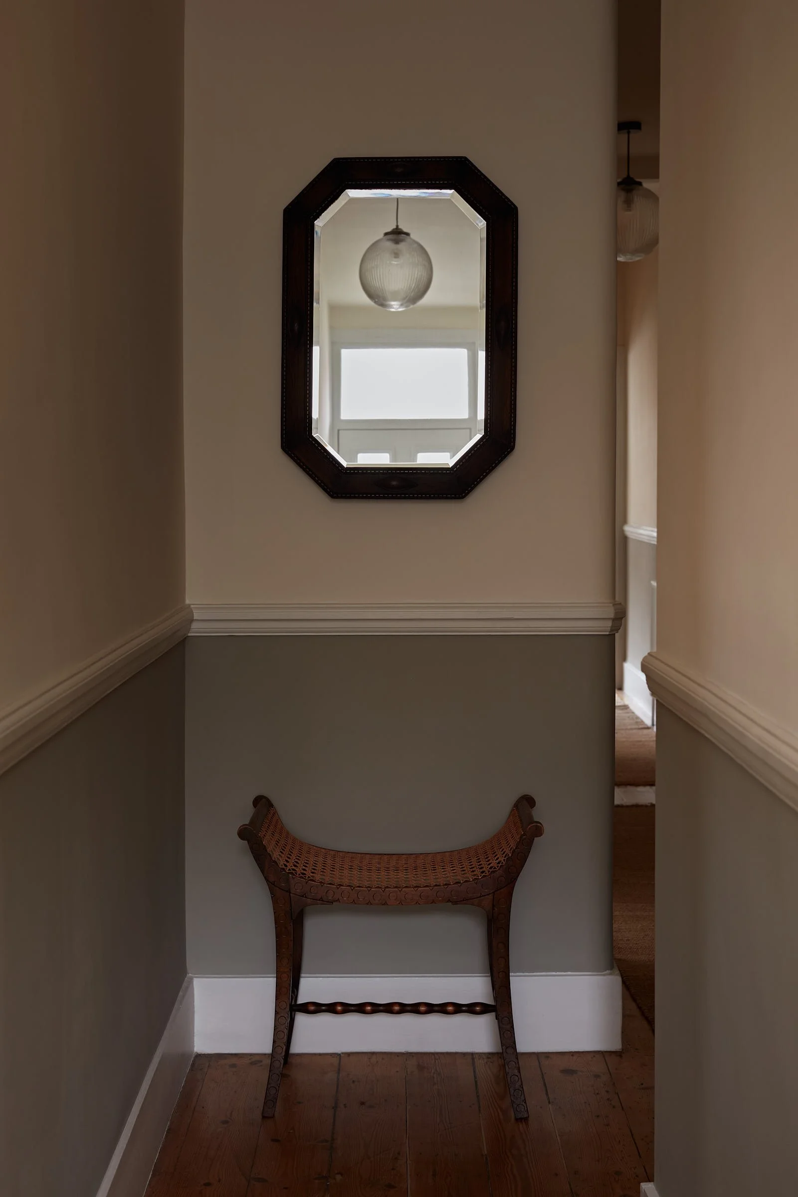 Hallway with a woven-seat bench beneath an octagonal timber mirror, designed by Partner London