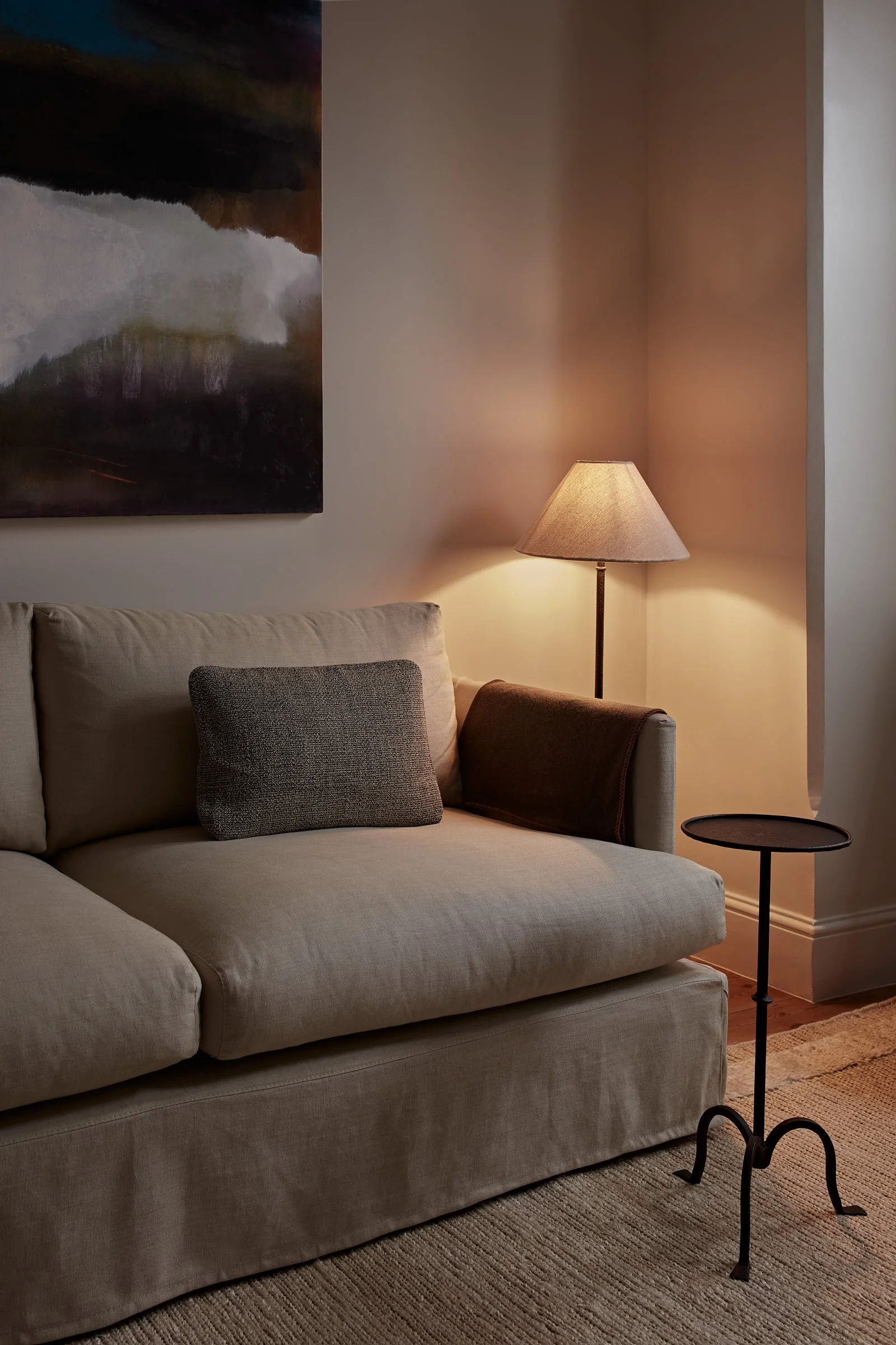 Calm sitting room corner with a linen sofa, floor lamp and large abstract painting over a woven rug