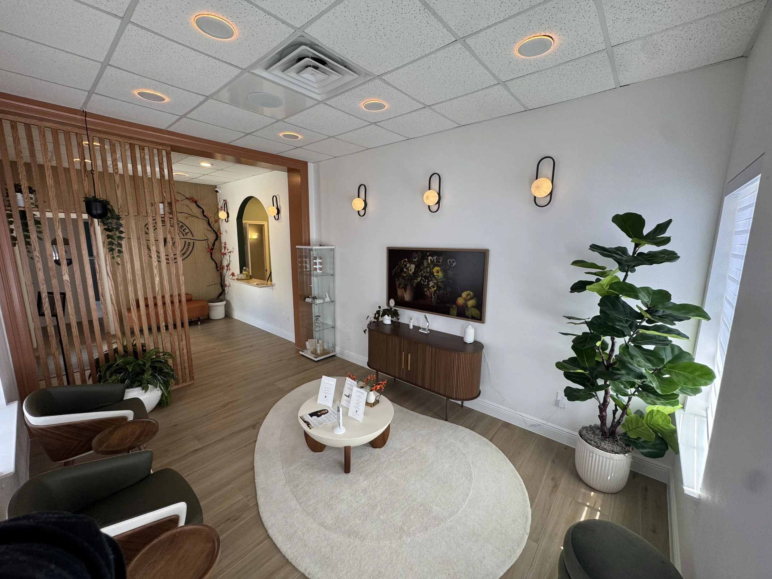 Medical or therapy room with treatment chair, chairs, plants, and medical equipment.