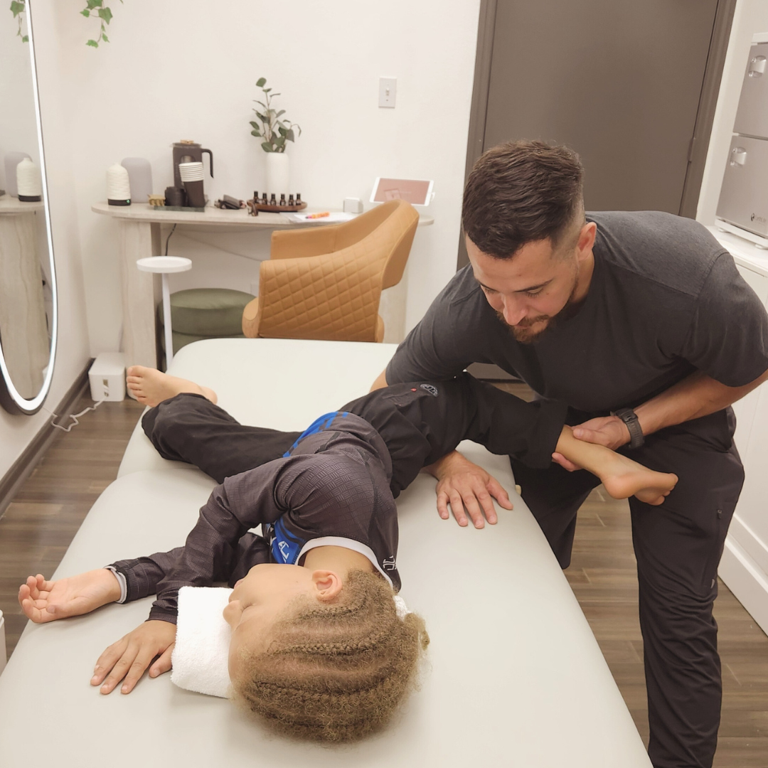 A physical therapist performs an ultrasound therapy on a woman lying on a treatment table in a clinic. The woman is wearing red leggings and a dark top, while the therapist is wearing black gloves.