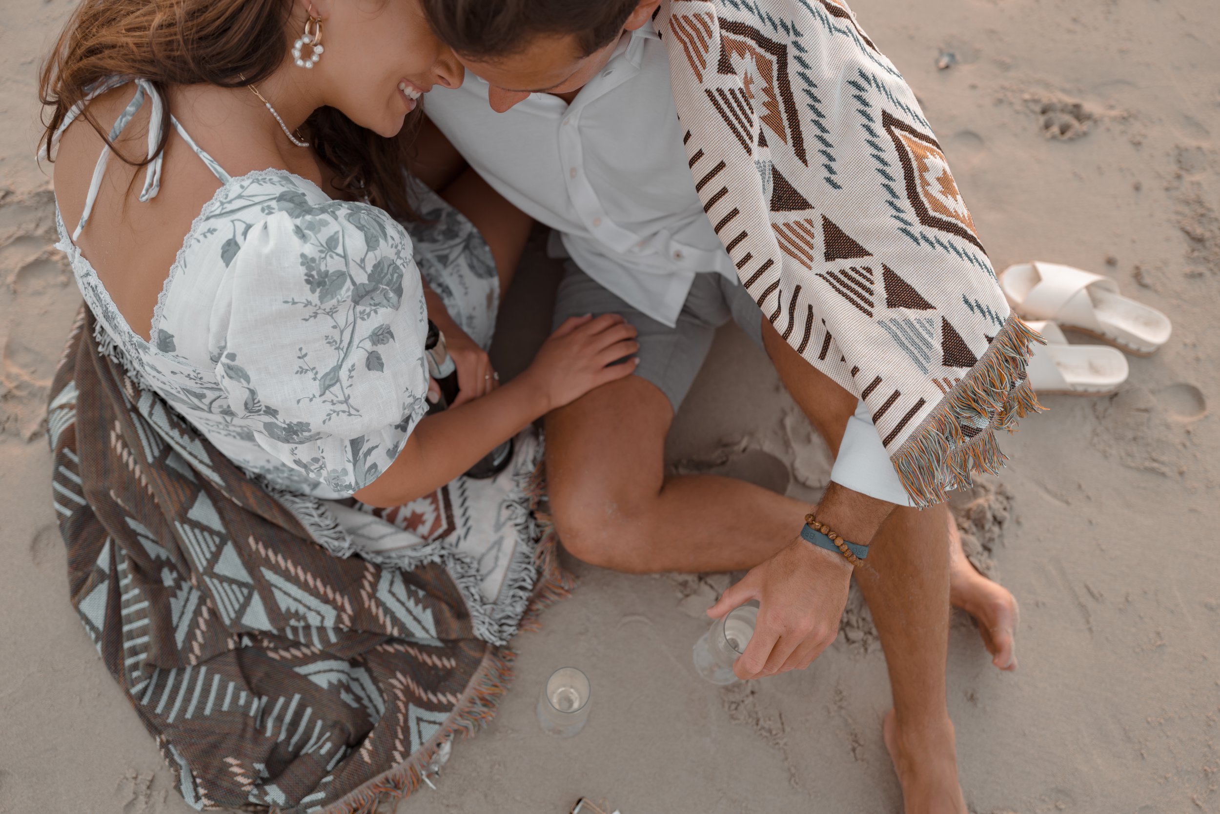 Intimate Beach Engagement: Bride Resting on Groom's Shoulder with Champagne Flutes and Blanket in New Jersey