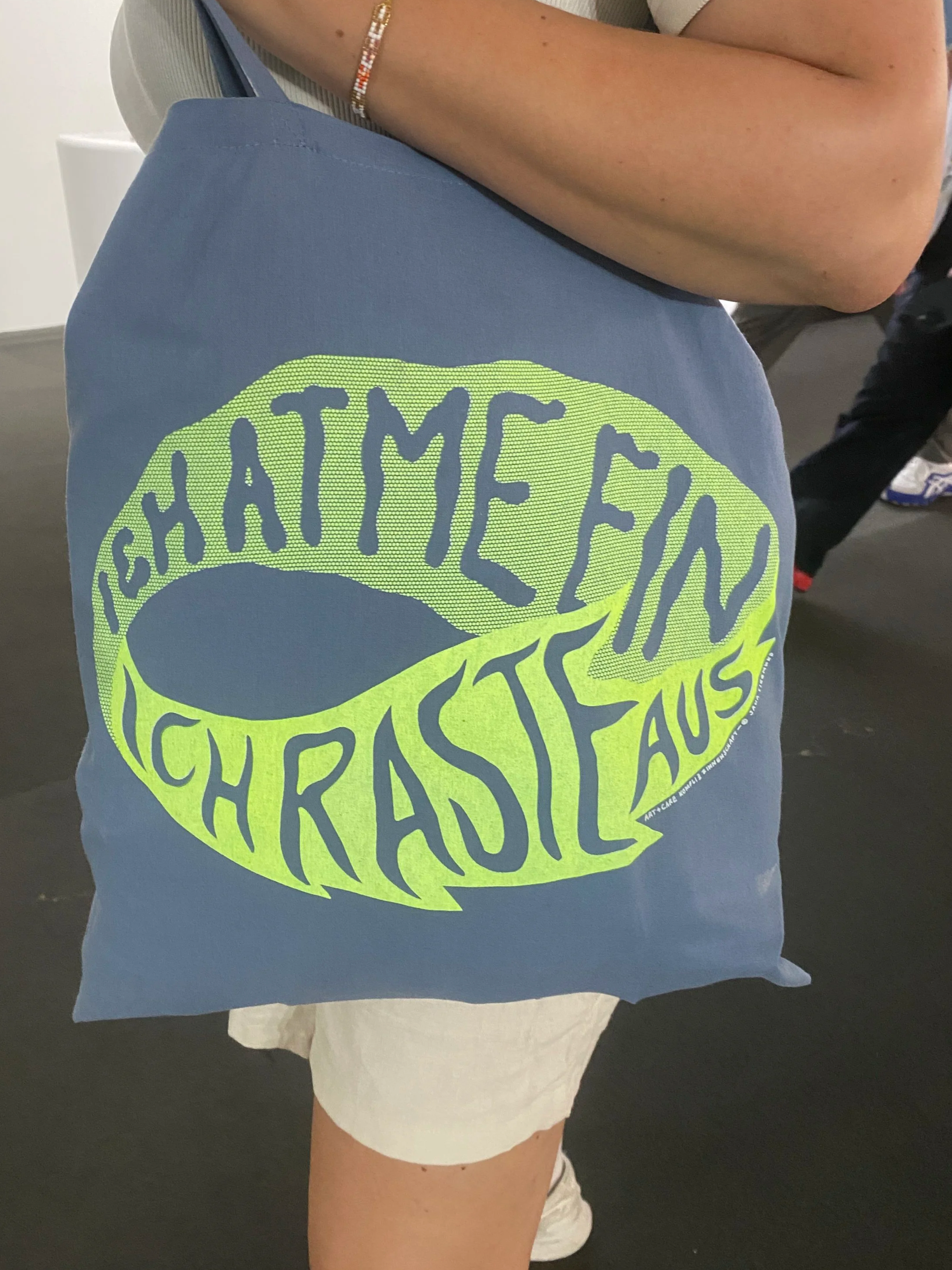 Person mit blauer T-Shirt, das den Schriftzug 'SATIE13' in gelber Farbe zeigt, sitzt auf einer weißen Krankenhausschaukel.