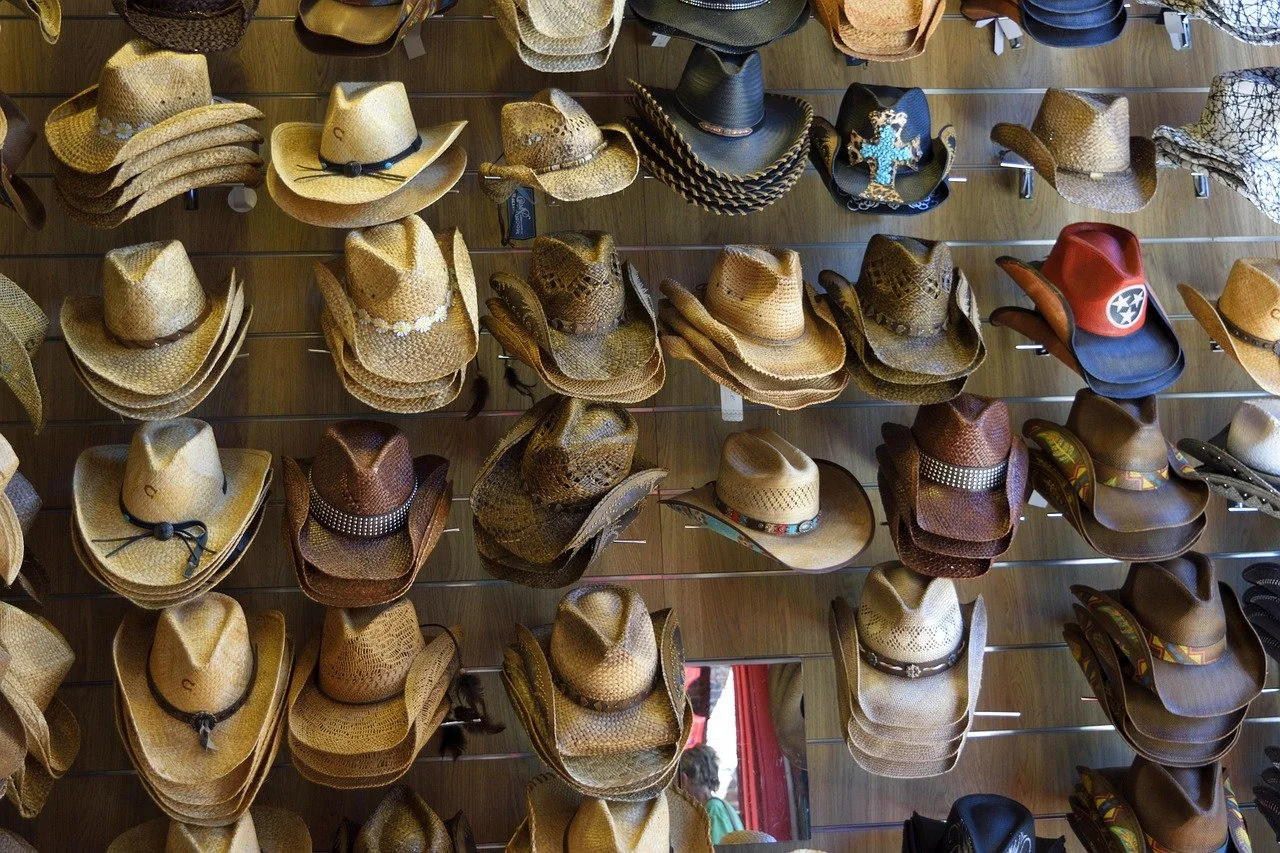 A display rack filled with various cowboy hats and a few baseball caps, mostly in shades of tan, brown, and black, with some hats decorated with bands or embellishments.