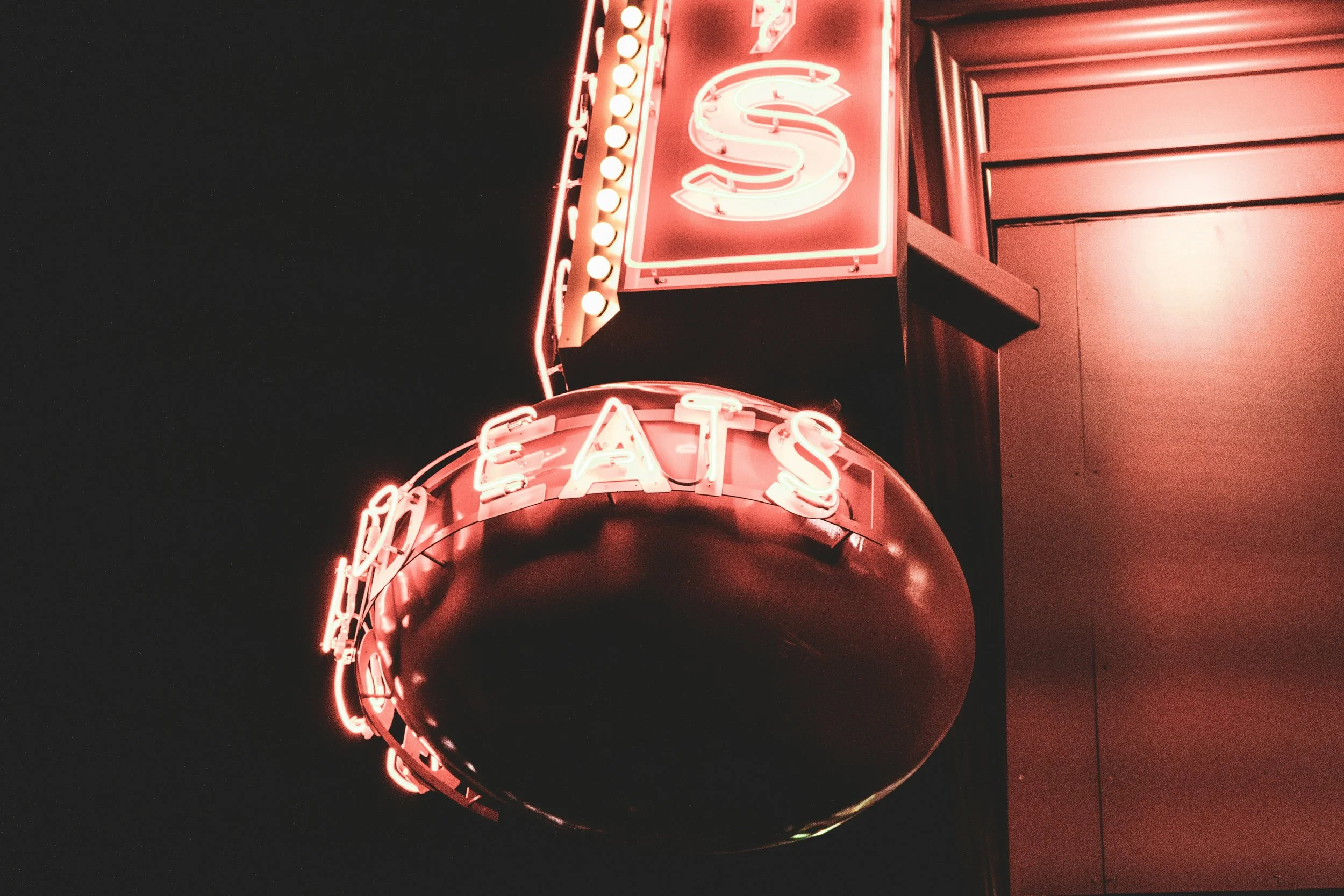 Red neon sign reading 'Eats' mounted on a building at night.