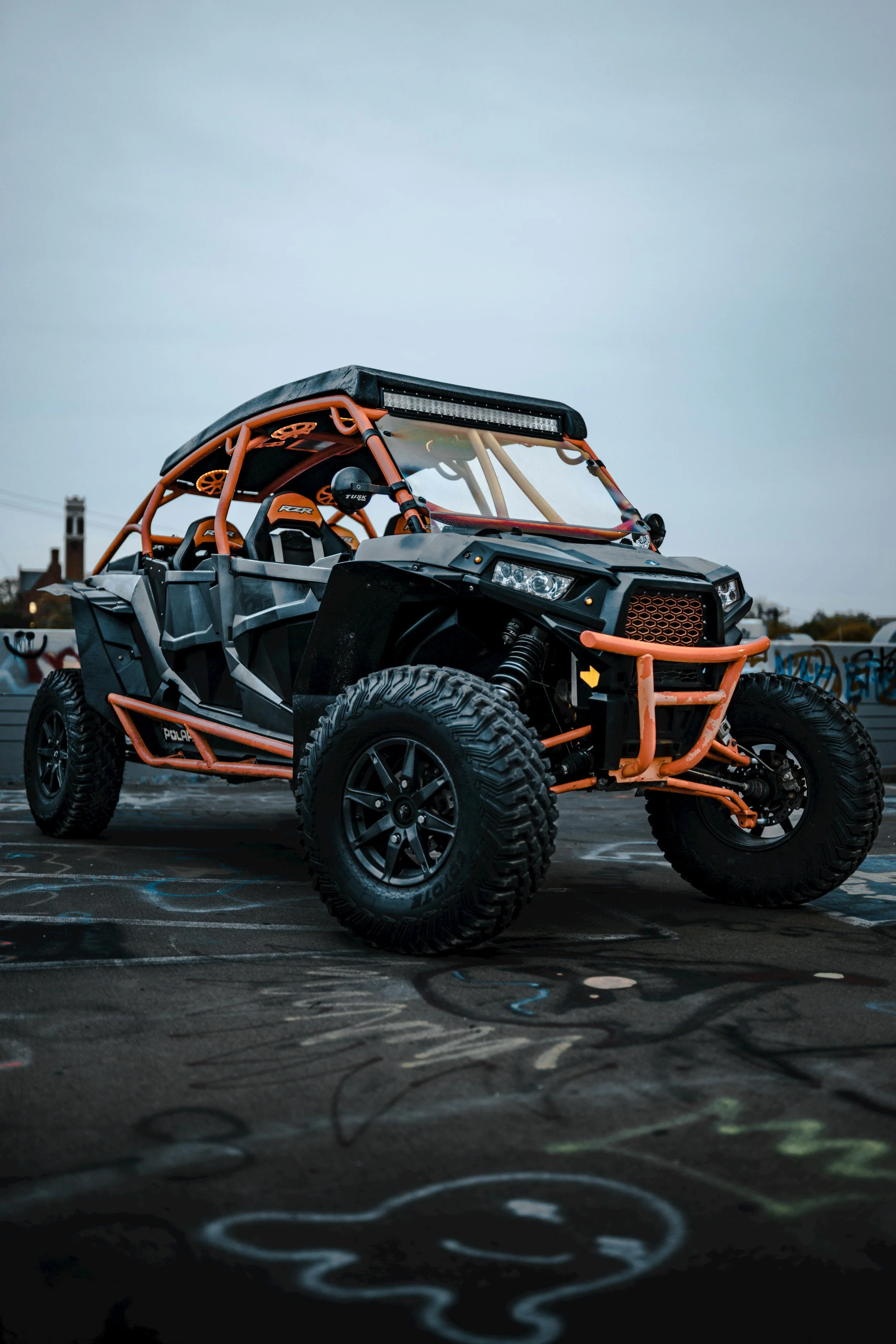Off-road utility vehicle parked on a graffiti-covered surface under a cloudy sky.