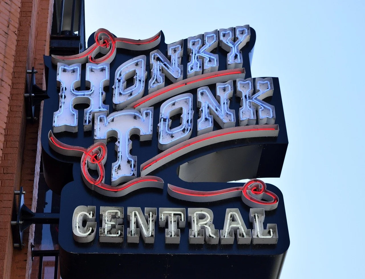 Neon sign reading 'Houston' above 'Central' against a blue sky, mounted on the side of a brick building.
