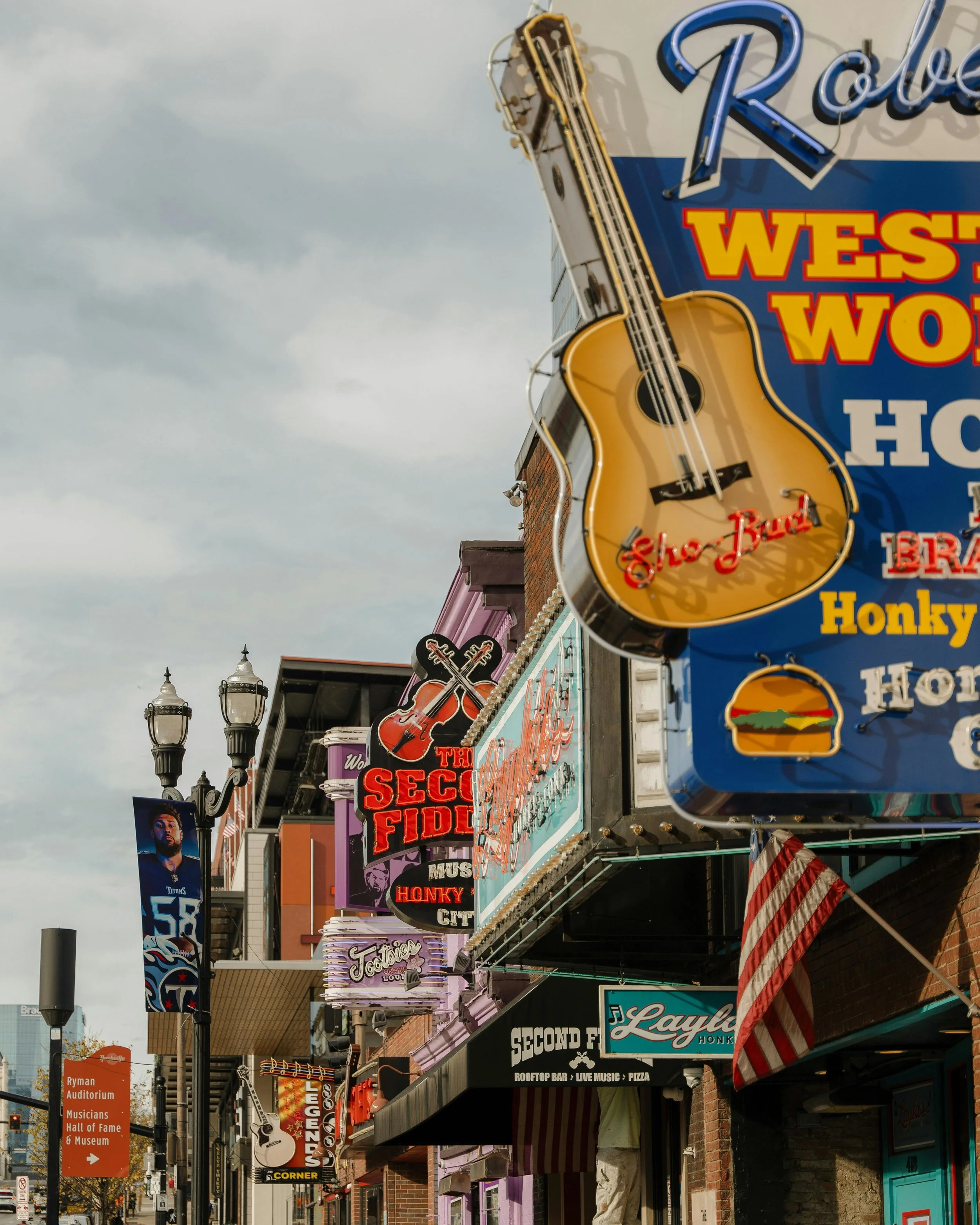 Street view of storefront signs and neon lights on a city street with cloudy sky in the background.