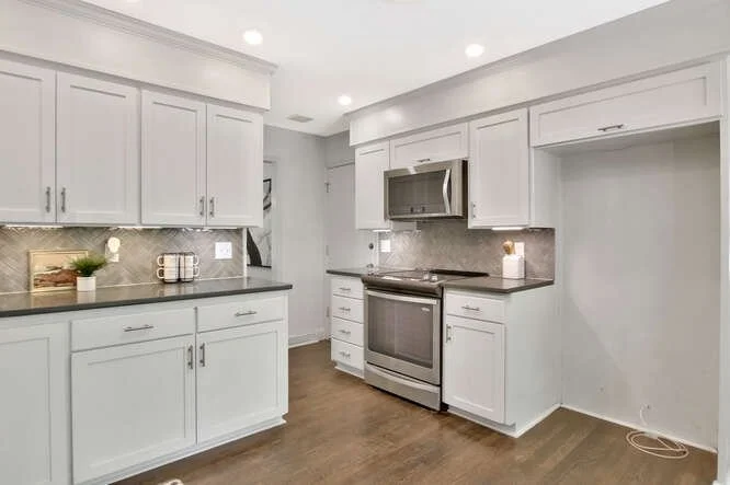 Modern kitchen with white cabinets, gray countertops, stainless steel appliances including stove and microwave, and hardwood floors.