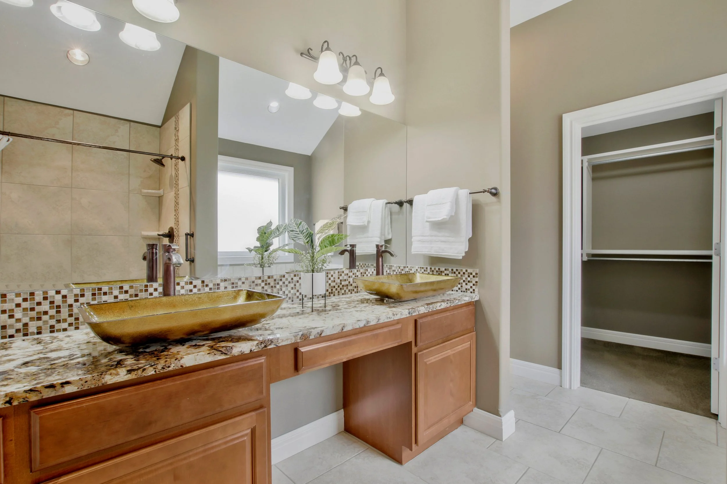 Bathroom with double vessel sinks with marble countertop, large mirror, towel rack, and a walk-in closet.