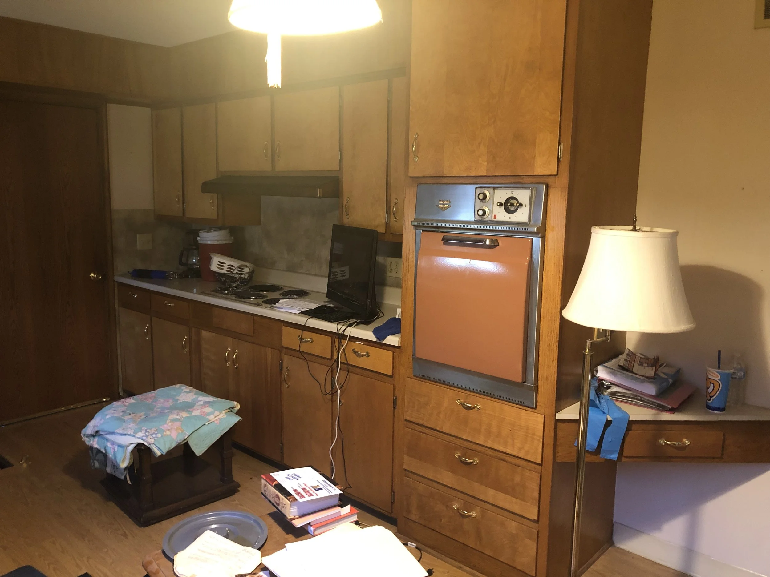 Kitchen with wooden cabinets, a small TV, a lamp, and various items on the counter and table.